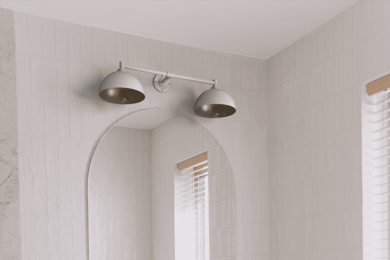 Silver gooseneck bathroom light mounted above a mirror, against beige tiled wall.