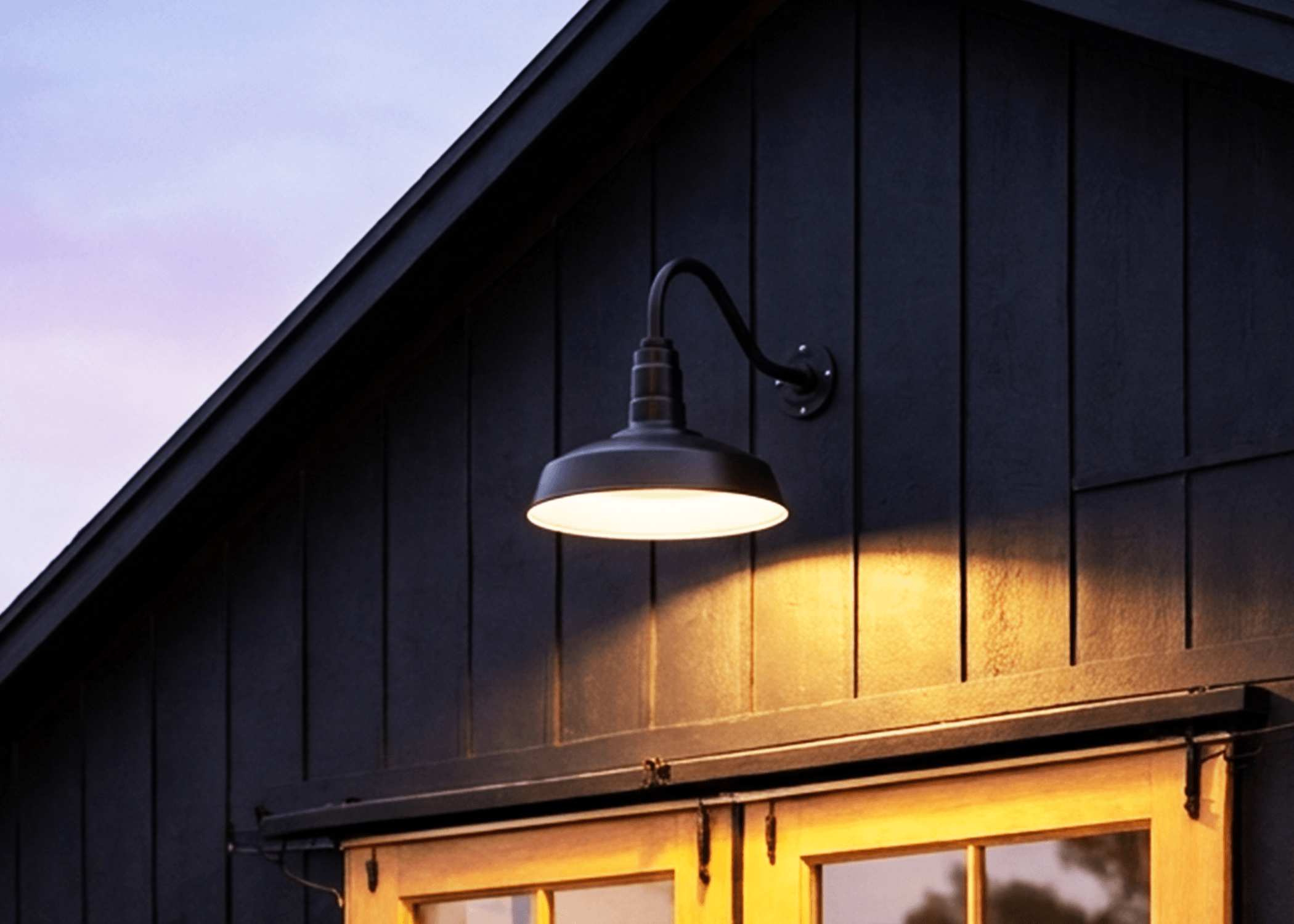 Barn-style gooseneck light on a dark farmhouse exterior at dusk