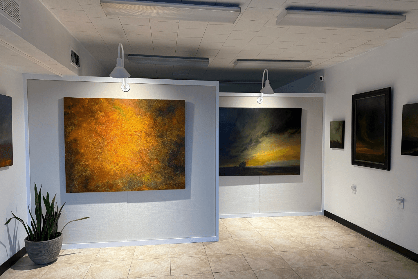 Art gallery with dramatic paintings illuminated by stylish gooseneck lights, adding depth and warmth to the display.