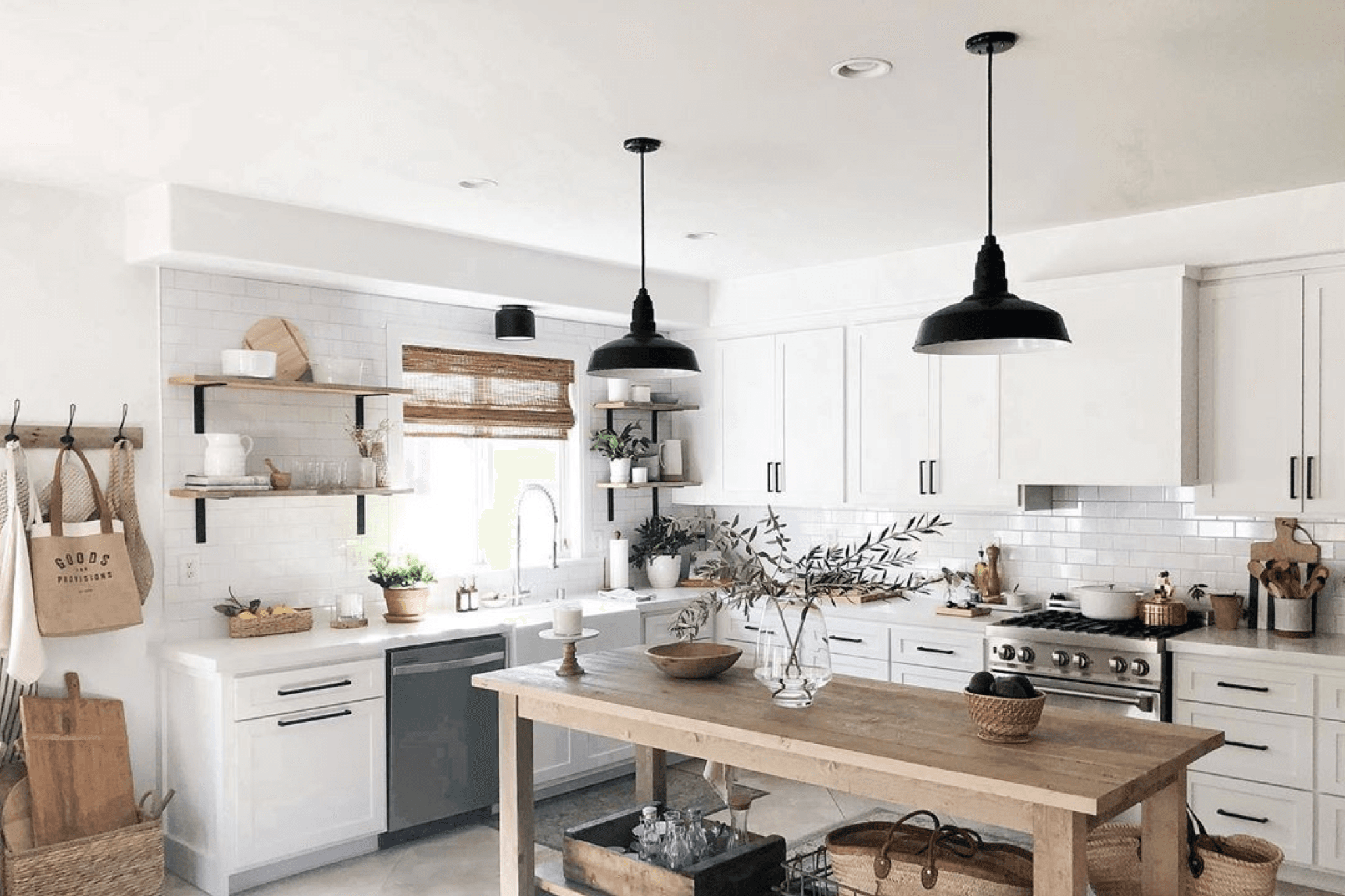 Modern kitchen with white cabinets, natural wood accents, and black pendant lights over a central island.