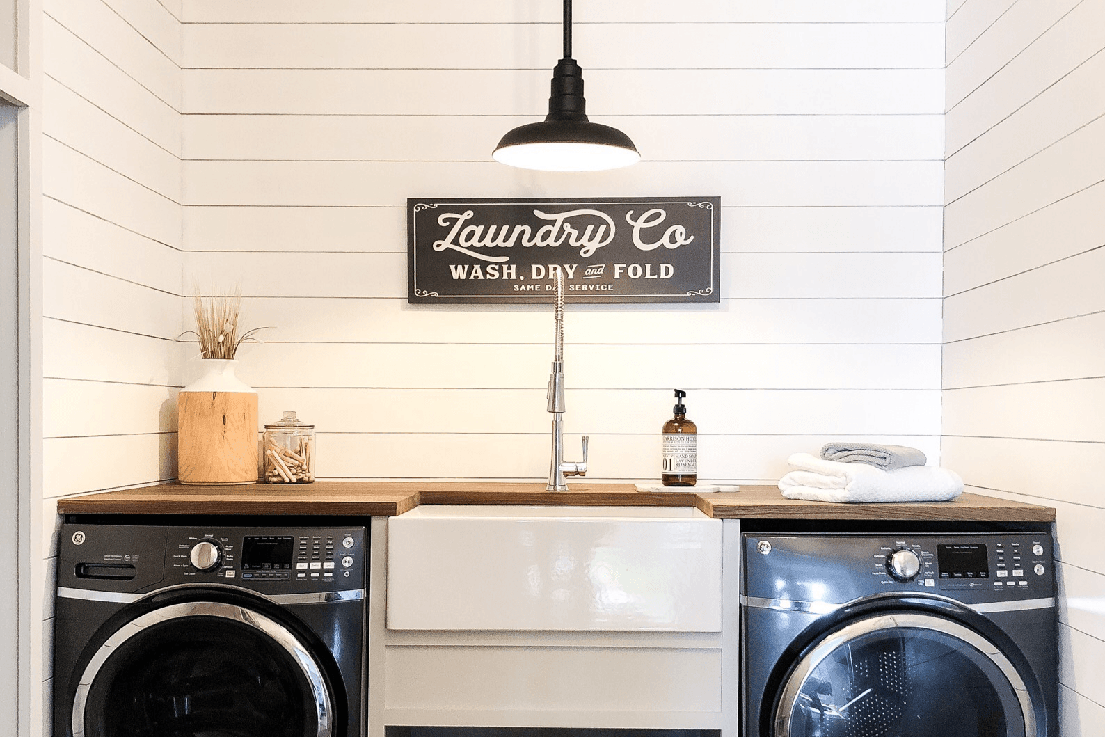 Laundry room with farmhouse sink, vintage wall sign, and pendant light fixture above washer and dryer.