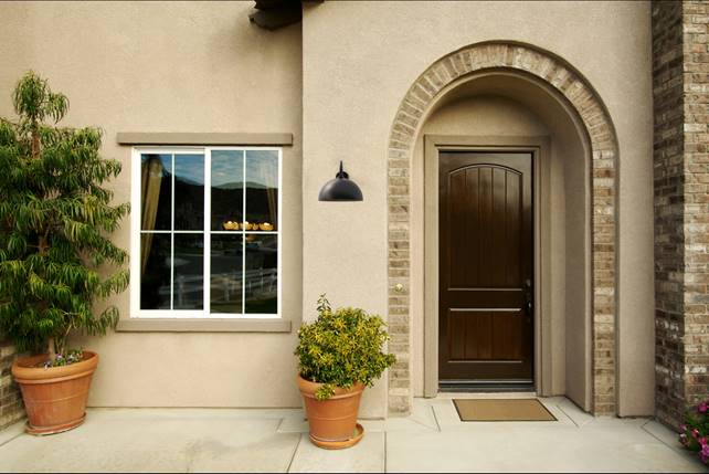 Exterior wall with a gooseneck outdoor light above the door, next to potted plants and a window.