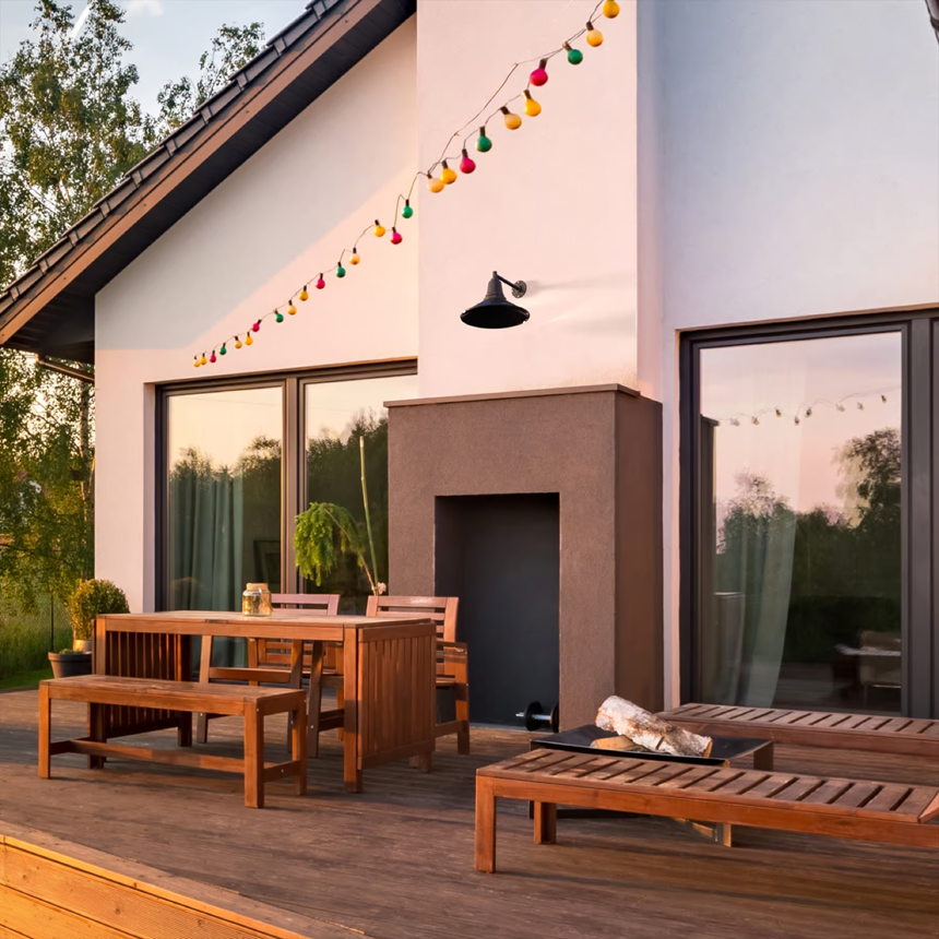 Outdoor patio with wooden furniture, string lights, and a black wall-mounted gooseneck light at sunset.